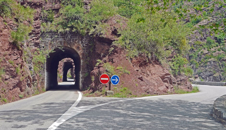 Picturesque mountain road with tunnel and directional signs on a sunny day.